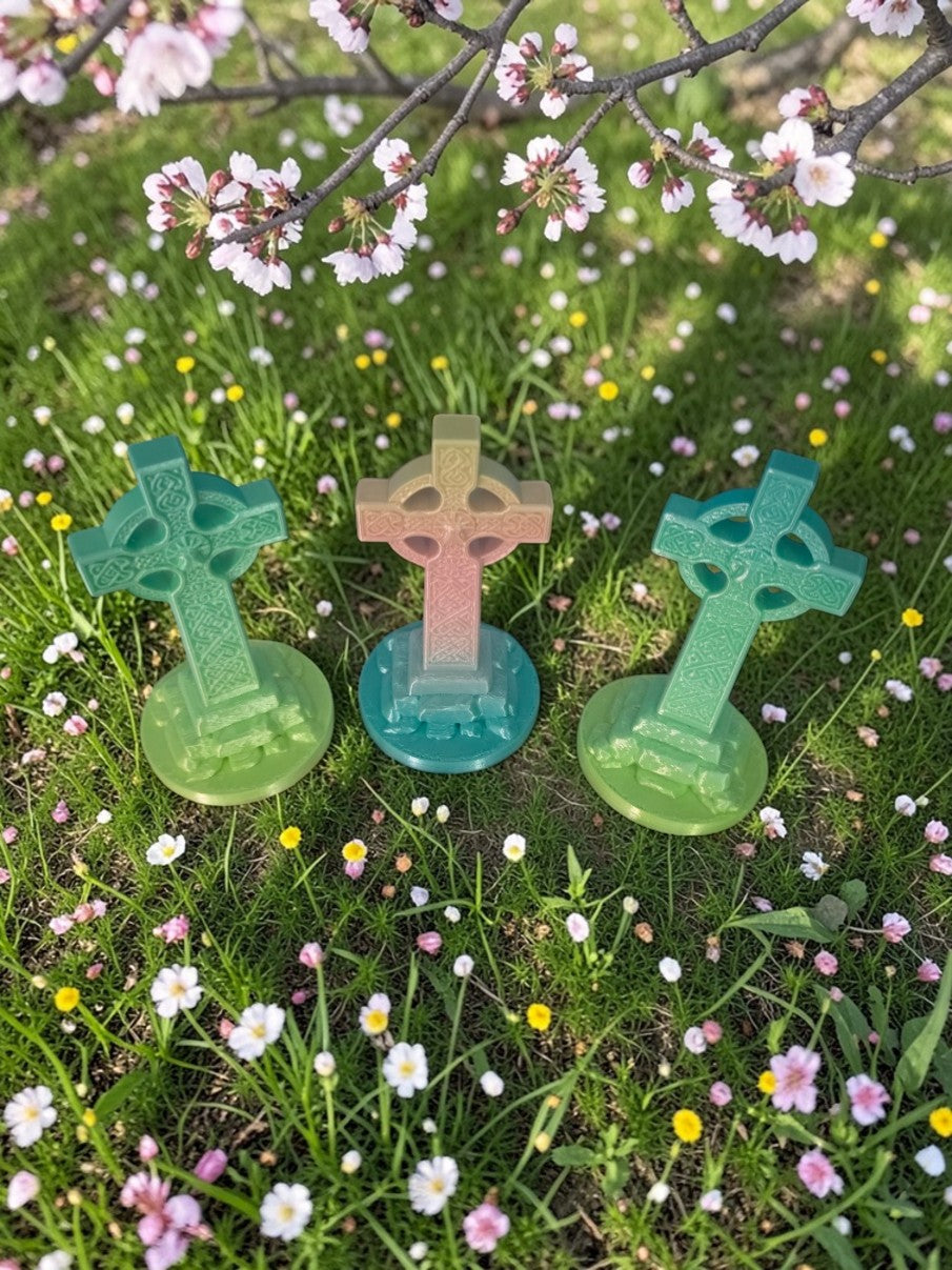 Three 3D printed Celtic Cross sculptures viewed from different angles outdoors beneath blooming tree branches with white and pink flowers.