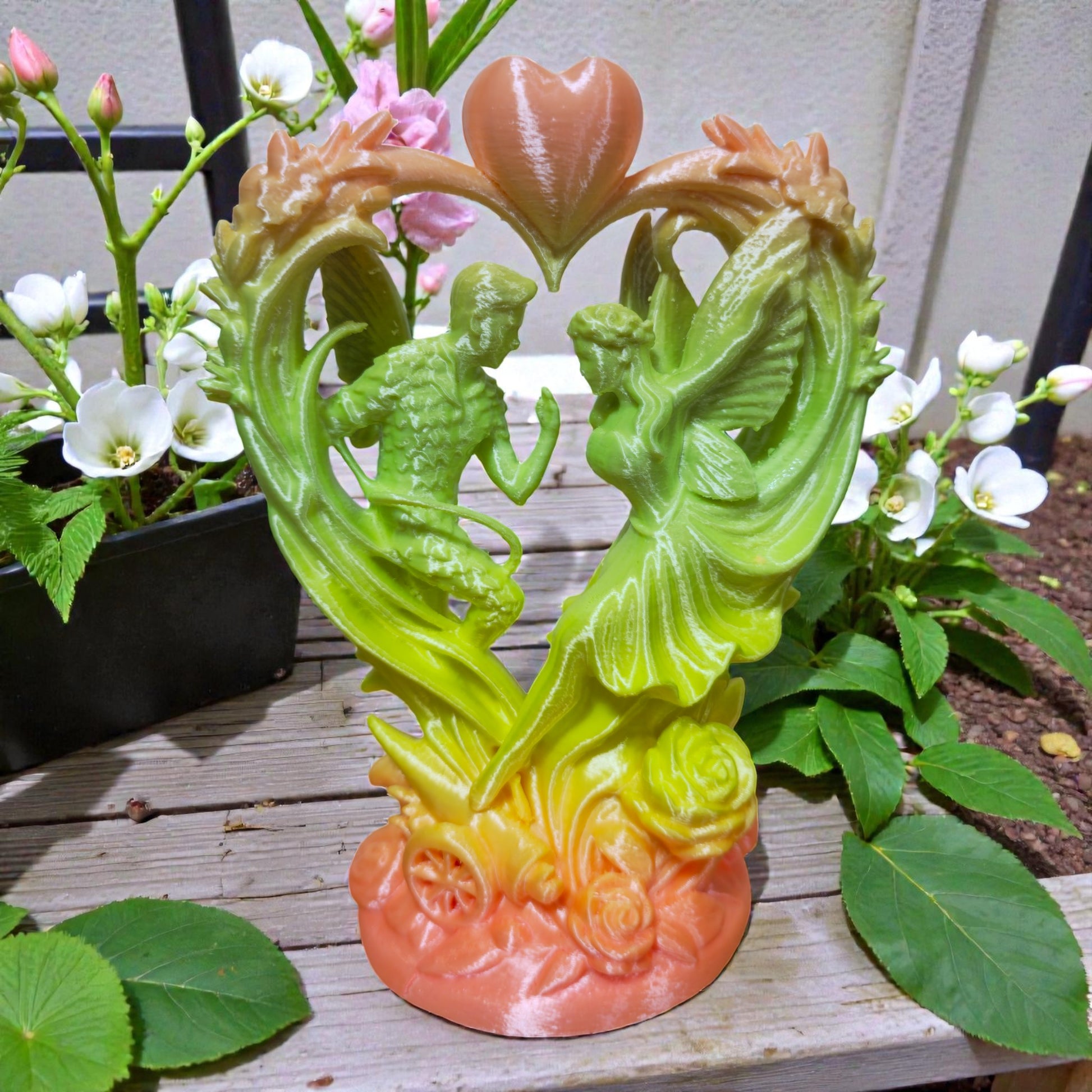 Front view of detailed angel couple within heart arch sculpture with floral and wheel accents in natural setting