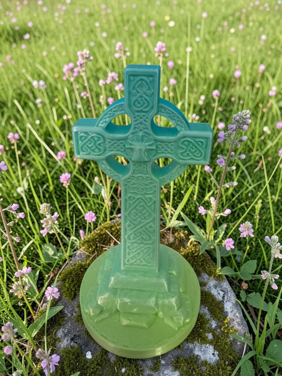 Front-facing Celtic Cross sculpture printed in green shades on stone surrounded by grass and wildflowers.